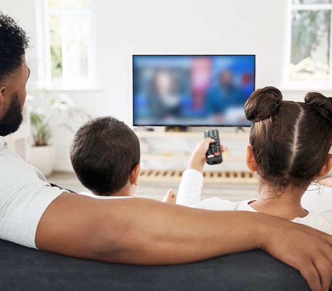 Family watching TV programming from their living room couch, viewed from behind