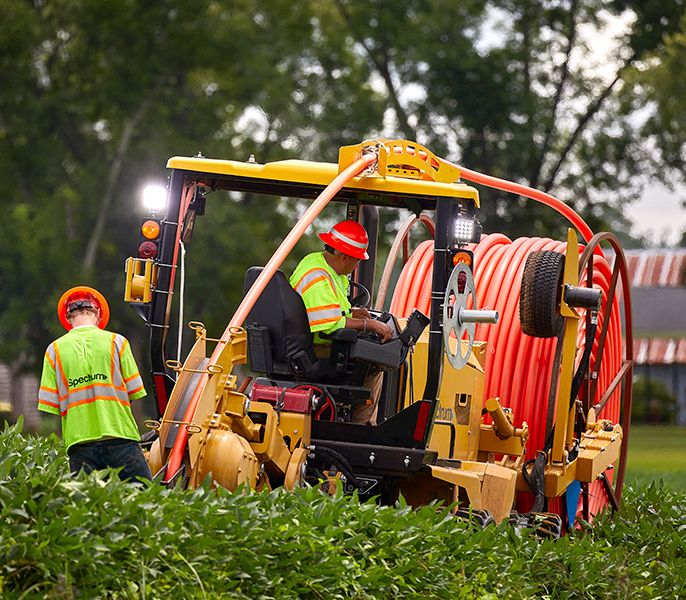 Spectrum technicians using a plow to bury fiber conduit during underground construction in a rural area
